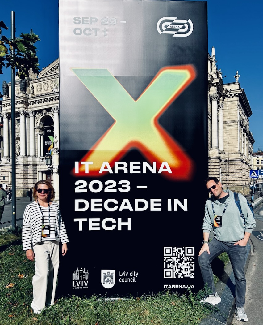 Two people beside the IT Arena 2023 “Decade in Tech” banner outside the Lviv Opera House