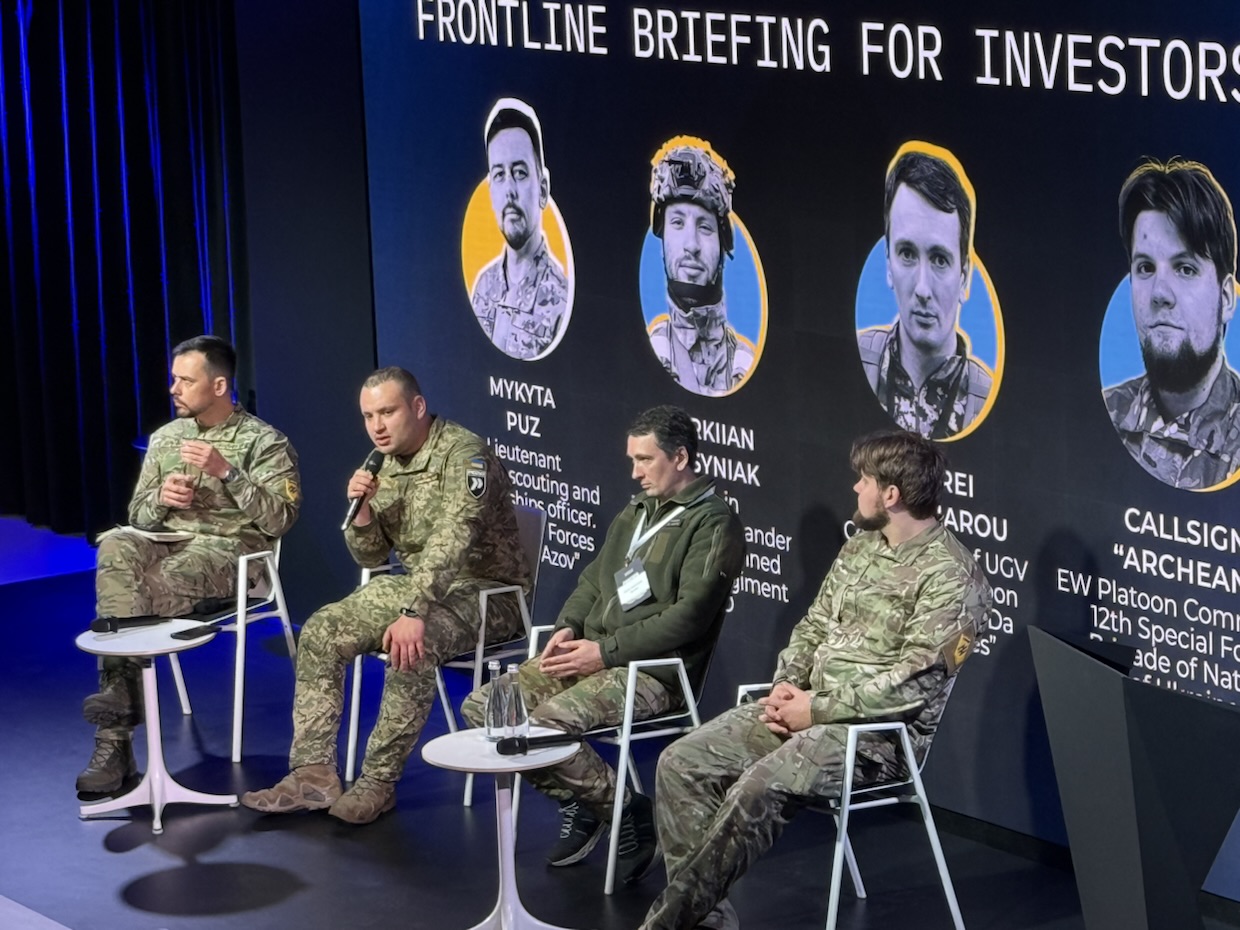 Ukrainian service members speaking on stage at a frontline briefing for investors